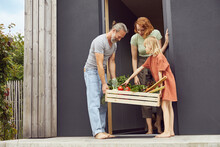 Woman Standing With Father And Daughter Carrying Vegetable Crate Outside Tiny House