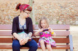 © xose casal/Westend61 - Mother and little daughter sitting together on a bench looking at cell phone