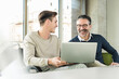 © UWE_UMSTAETTER/Westend61 - Happy mature businessman and young man in wheelchair using laptop in office