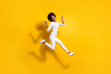 Full size profile side photo of dark skin girl run jump up show v-sign isolated on shine yellow color background