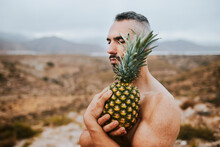 Man Holding Pineapple In Field During Sunset