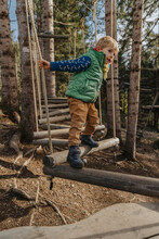 Boy Holding Rope While Walking On Wood In Forest At Salzburger Land, Austria