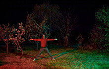 Man With Arms Outstretched Standing In Garden At Night