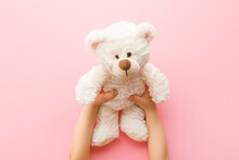 Smiling White Teddy Bear In Baby Girl Hands On Light Pink Background. Pastel Color. Closeup. Point Of View Shot. Kids Best Friend. Top Down View.