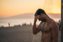 Shirtless Man Taking Shower At Beach Against Sky During Sunset