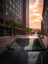 Sunrise Between Red Buildings On Summer Street In Boston, Massachusetts. Abstract Building Reflections Over The Car Parked On The Street In Downtown Boston.