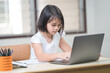 © EduLife Photos - Asian children girl student writing on notebook while studying online via laptop while at home. Education Concept Stock Photo