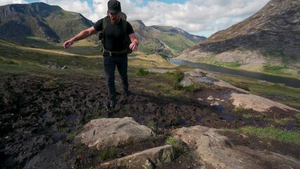 Canvas Print - A man in the mountains walking through thick mud with a backpack