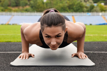 Poster - Young woman doing plank exercise at stadium