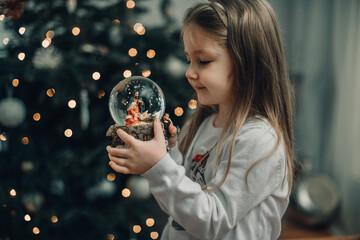 Girl looking at a glass ball with a scene of the birth of Jesus Christ in a glass ball on a Christmas tree