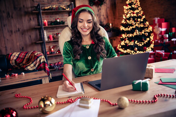 Poster - Photo of positive young woman santa helper sit table laptop make list write xmas christmas indoors inside house home