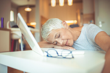 Fototapete - Menopausal mature woman at work feels bad, depression of strength and having a rest. She is sleeping in the workplace at the table before laptop. I don't have the energy to get through these deadlines