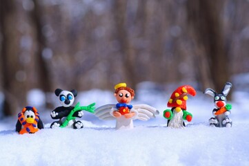 Wall Mural - Figurines of fairy-tale characters in the winter forest. An angel with a gift, a dwarf, a rabbit with a carrot, a panda, a penguin in a scarf.