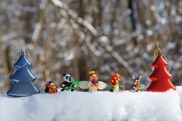 Wall Mural - Figurines of fairy-tale characters in the winter forest. An angel with a gift, a dwarf, a rabbit with a carrot, a panda, a penguin in a scarf. There are toy Christmas trees nearby.