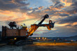 © saravut - The worker man and Yellow excavator loading soil a truck at mine back lit on twilight after sunset