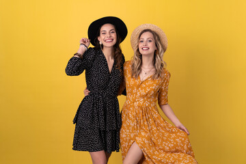 beautiful women friends together isolated on yellow background in black and yellow dress and hat