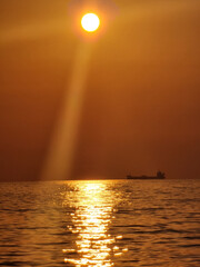 Poster - Vertical shot of a shiny sea with a silhouette of a boat under a red sky at sunset