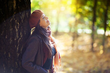 Girl In An Beret Stands Next To A Tree On A Sunny Autumn Day