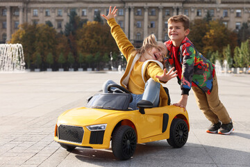 Cute boy pushing children's car with little girl outdoors on sunny day