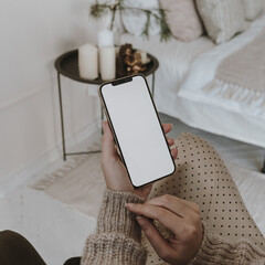 Wall Mural - Mobile phone with blank screen in female hand. Woman sitting in bright cozy bedroom. Aesthetic elegant social media, blog, message concept. Mockup copy space template