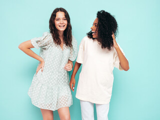 Two young beautiful smiling international hipster female in trendy summer clothes. Sexy carefree women posing near blue wall in studio. Positive models having fun. Concept of friendship