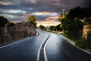 Wall Mural - Views of the stone paved road leading from the entrance gate of the ancient city of Side towards the city center. Cloudy Sunset Sky and Sea view.