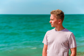 Wall Mural - A young blond man walks on the beach near the azure ocean or sea. The concept of a happy summer vacation