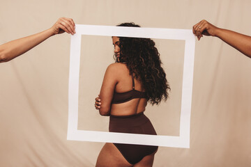 Young woman standing behind a picture frame in brown underwear