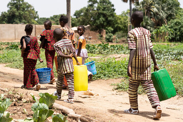 Wall Mural - Group of black African children carrying empty water containers on their way home from the village well after helping to water the fields