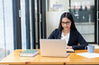 © ArLawKa - Confident Asian woman working on laptop and reading paper documents at home. A cheerful woman in a suit sits at her desk in the office.