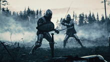 Dark Age Battlefield: Two Armored Medieval Knights Fighting With Swords. Battle Of Armed Warrior Soldiers, Killing Enemy In Mysterious Forest. Cinematic Smoke, Mist, Light In Historic Reenactment
