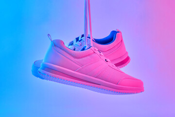 Wall Mural - Hand hold white sneakers in neon light. Sport shoes for training in the gym. Creative minimalism. 90s concept.