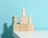 Fototapeta Do przedpokoju - wooden figures of men stand on a pedestal of their cubes on a blue background. The concept of rivalry in sports, business and life. Achieving success and leadership