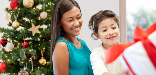 Poster - winter holidays, family and people concept - happy mother and daughter with gift at home over christmas tree background