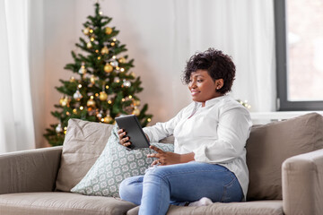 Wall Mural - technology, people and winter holidays concept - smiling african american woman with tablet pc computer on christmas at home