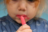 A little girl tries to put on her lips with lipstick and smears the paint out of ineptitude.