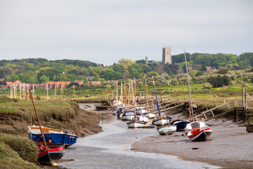 Wall Mural - Boats stranded during low tide with Quay and Blakeney village and Church in the background North Norfolk, British Summer, low tide, boat on the shore