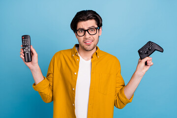 Sticker - Photo of uncertain puzzled guy hold remote control gamepad make choice wear yellow shirt isolated blue color background