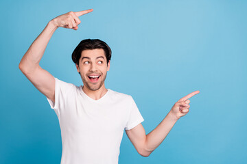 Poster - Photo of excited guy indicate fingers empty space look side wear white t-shirt isolated blue color background