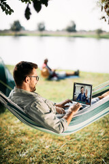 Wall Mural - happy man uses laptop and makes video call with his co-worker while camping in nature.