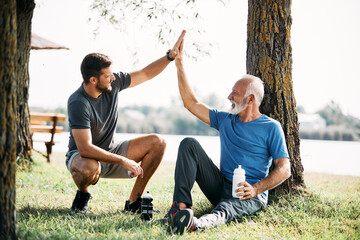 Wall Mural - Happy senor athlete and his son greet with high-five after sports training in nature.