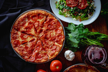 Wall Mural - Closeup top view of a delicious pizza pepperoni and a salad  on a table with other ingredients