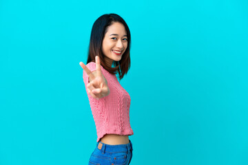 Wall Mural - Young Vietnamese woman isolated on blue background smiling and showing victory sign