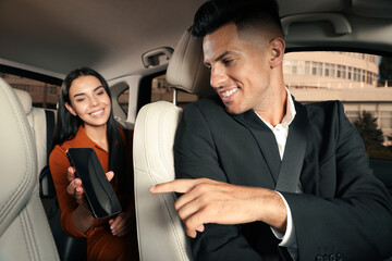 Wall Mural - Young woman showing smartphone to taxi driver in modern car