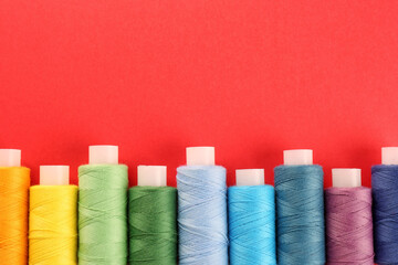 Poster - Different colorful sewing threads on red background, flat lay. Space for text