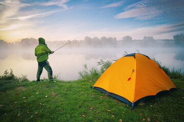 Wall Mural - Fisherman by lake with orange tent on foggy morning