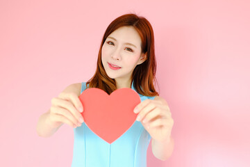 Portrait beautiful asian woman on pink background, valentine day in love concept, model holding red heart sign in hand