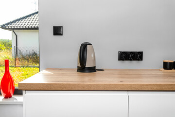 Wall Mural - An electric kettle standing on the countertop on the kitchen cabinets visible a large window in the dining room and red vase.