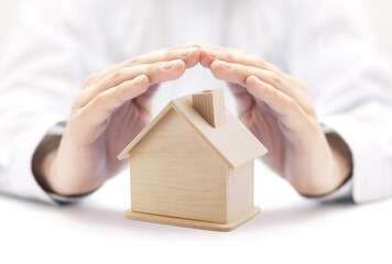 Poster - Wooden house shape protected by hands. Home insurance concept