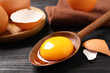 Spoon with raw egg yolk on black wooden table, closeup
